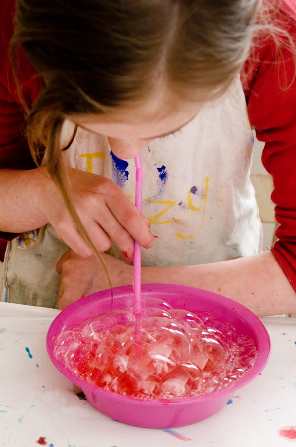 child blowing bubbles in bowl of paint