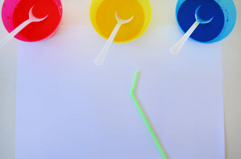 3 bowls of paint with spoons, a sheet of paper and a straw