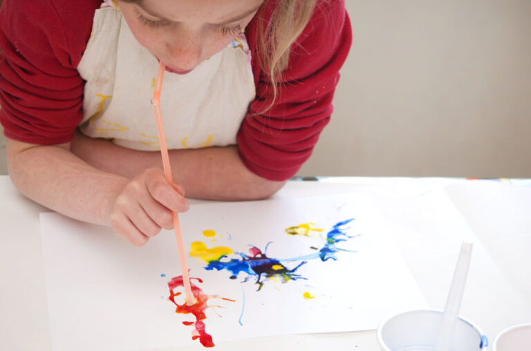 child blowing paint with a straw