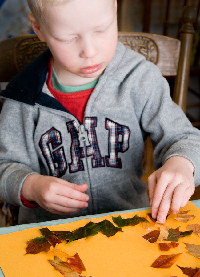 toddler sticking leaves to orange paper
