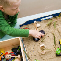 preschooler playing with sand and cars in a tray