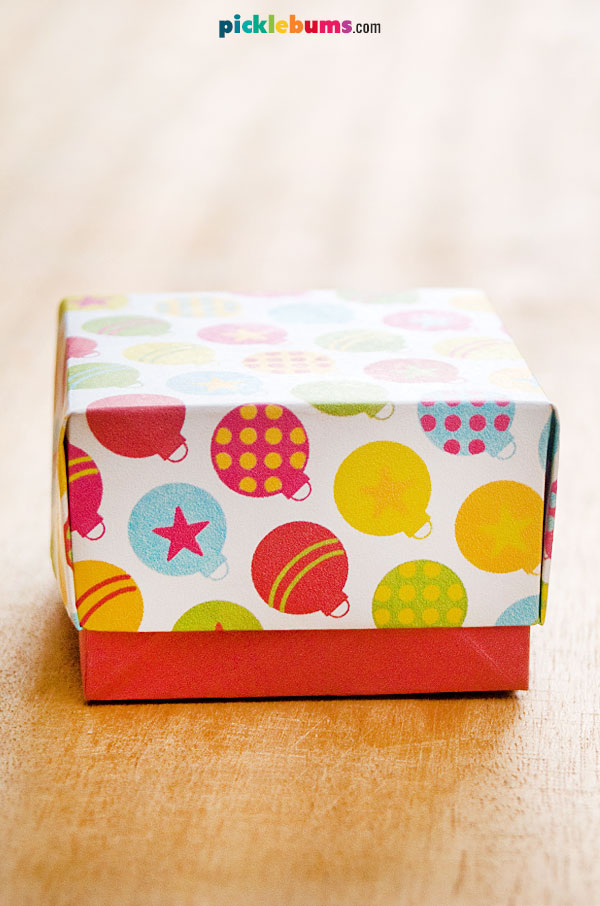 paper gift box with red bottom and coloured Christmas baubles on top