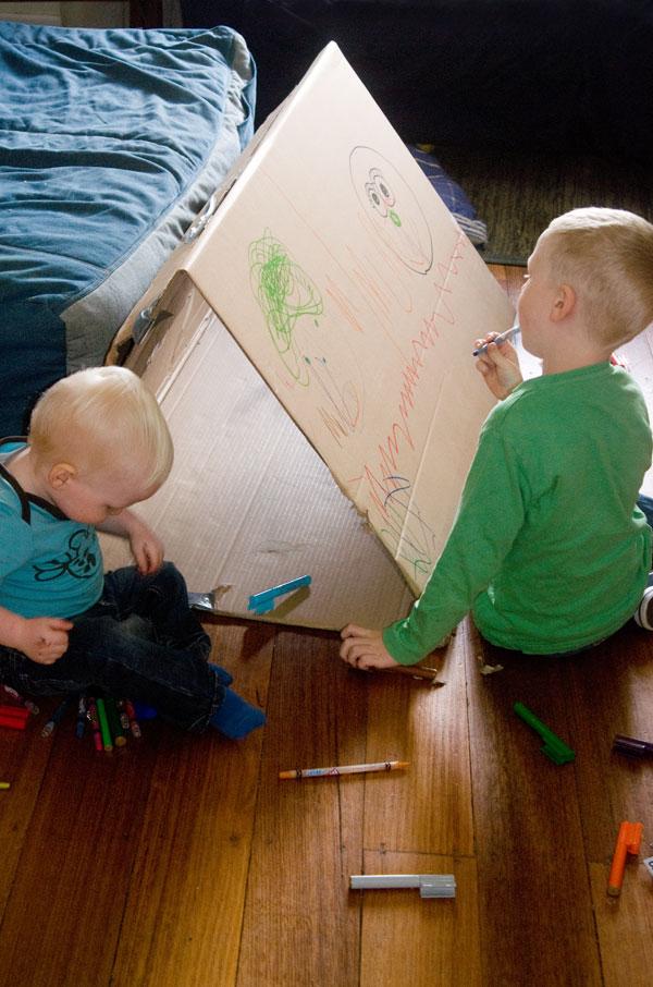 two kids drawing on cardboard tunnell